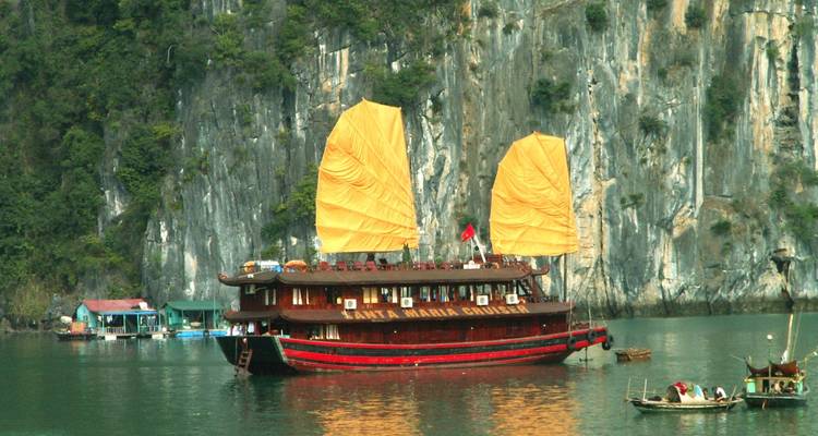 Traditionelles vietnamesisches Boot mit orangen Segeln in einer ruhigen Bucht.