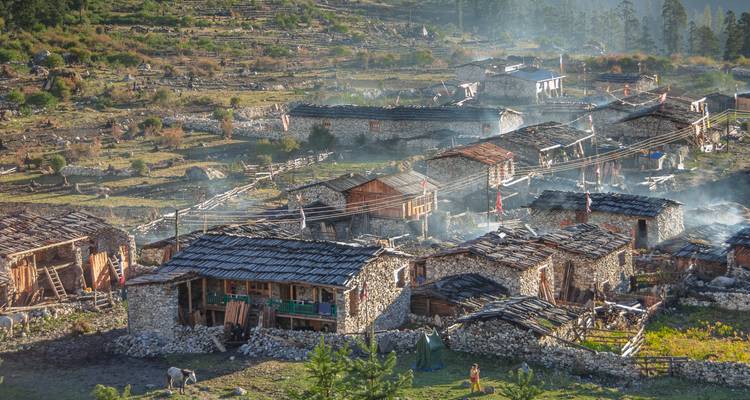 Rustiek bergdorp met stenen huizen en rook die uit de schoorstenen opstijgt.