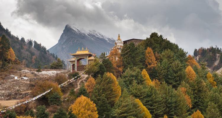 Ein traditionelles Kloster inmitten bunter Herbstbäume vor einer Bergkulisse.