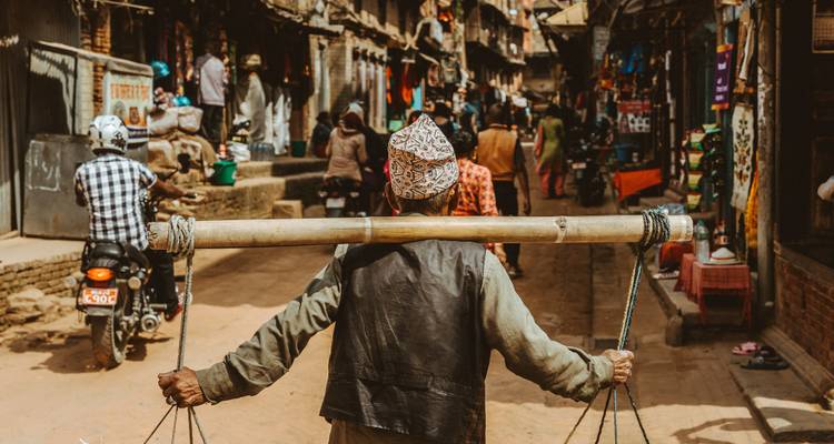 Een man die goederen draagt aan een stok lopend door een levendige straatmarkt.
