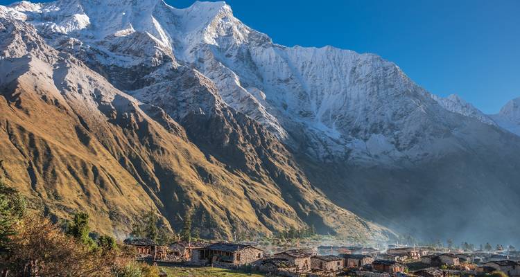 Dorf eingebettet in einem Tal mit sich erhebenden schneebedeckten Bergen als Kulisse.