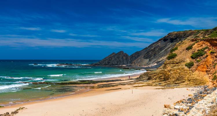 Playa salvaje de arena blanca bordeada por acantilados rocosos y olas color turquesa bajo un cielo azul brillante