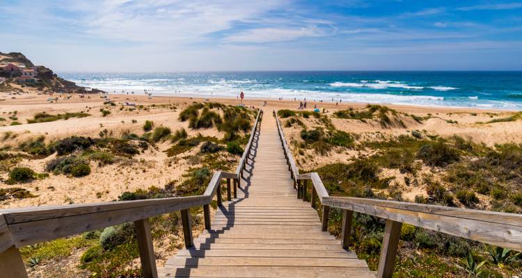 Pasarela de madera que atraviesa las dunas hacia una amplia playa del Atlántico con olas rodantes