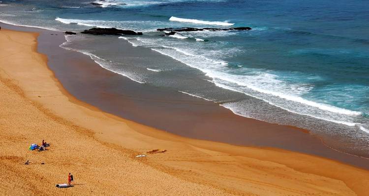 Vista aérea de una amplia playa arenosa con algunos bañistas y olas suaves llegando a la orilla