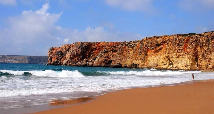 Playa de arena dorada con olas chocando contra acantilados naranjas del mar muy altos