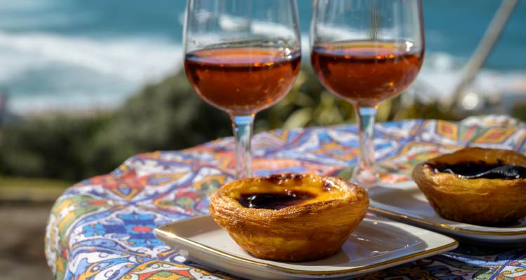 Pastéis de nata and glasses of port wine on a colorful tiled table overlooking the Atlantic.