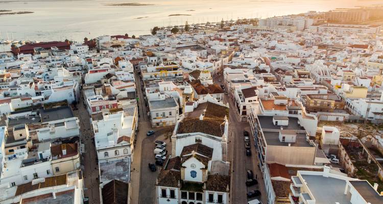 Drone shot of Faro’s whitewashed old town and marina bathed in warm evening light.