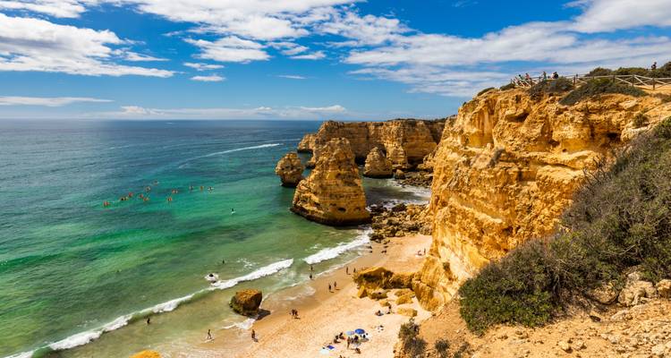 Vibrant view of Praia da Marinha cliffs with emerald sea, beachgoers and kayakers below.
