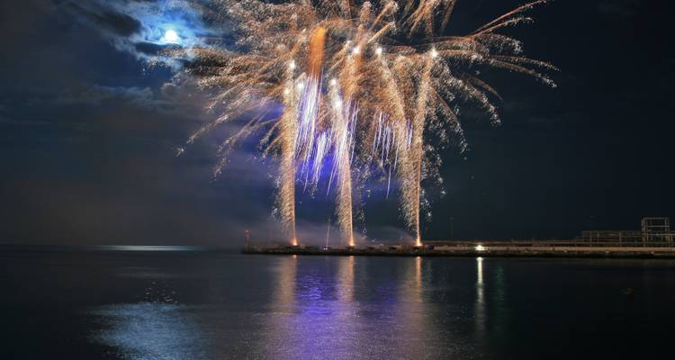 Nachtelijk vuurwerk dat explodeert boven water met reflecties op de kalme zee.