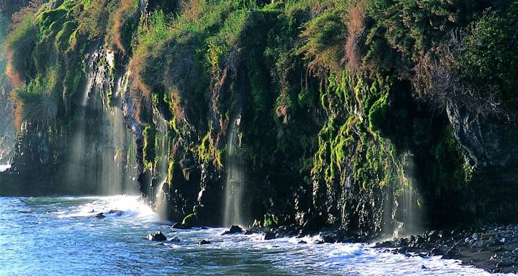 Klif met watervallen en groen naast de oceaan.