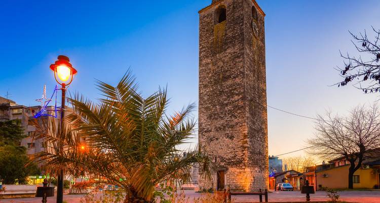 Torre de reloj de piedra alta en una plaza pública al atardecer.