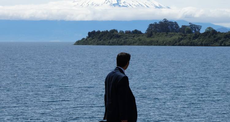 Homme en costume regardant à travers un lac vers une montagne enneigée.