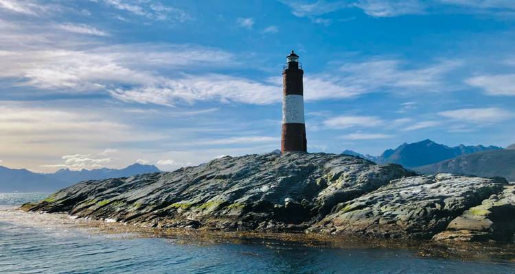 Leuchtturm auf einer felsigen Insel mit Bergkulisse