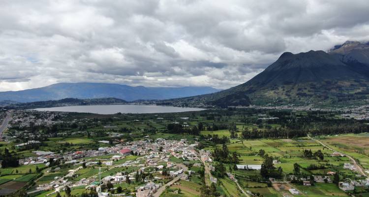 View of a town near a lake with mountains under a cloudy sky.