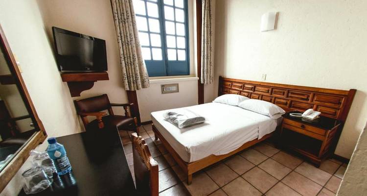 Einfaches Hotelzimmer mit einem Einzelbett und Schreibtisch.