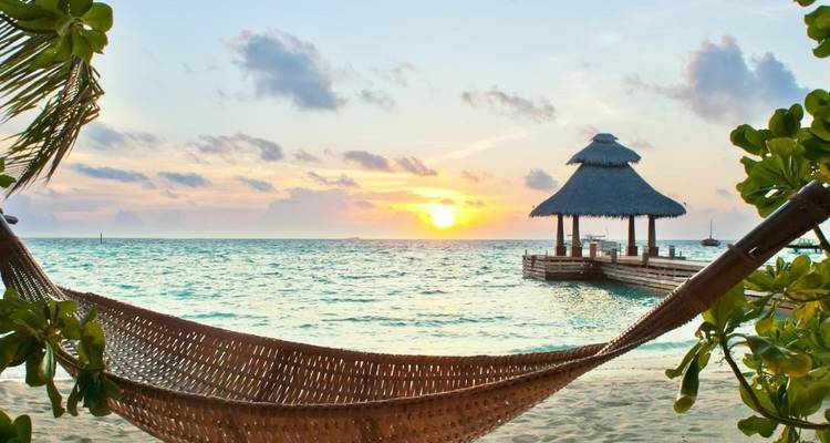 Zonsondergangzicht over de oceaan met een hangmat en een rieten prieel.