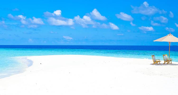 Ongerept wit zandstrand met heldere blauwe lucht en oceaan.