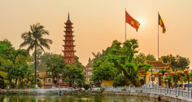 Tempel mit Flaggen bei Sonnenuntergang, der sich im Wasser spiegelt.