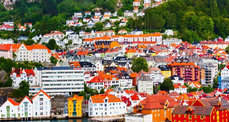 Panoramisch uitzicht op dicht opeengepakte, felgekleurde huizen die langs een groene helling in Bergen, Noorwegen omhoog klimmen.
