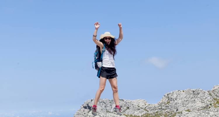 Femme sautant de joie sur un terrain rocheux sous un ciel bleu.