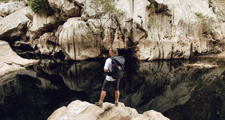 Une personne debout près d'une surface d'eau réfléchissante dans une zone rocheuse.