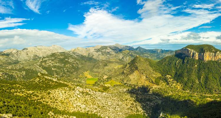 Vue panoramique de vallées verdoyantes et de montagnes sous un ciel bleu.