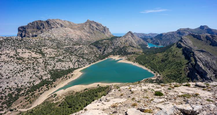 Blick von einem hohen Grat auf die türkisfarbenen Gewässer des Stausees Cúber, umgeben von felsigen Gipfeln Mallorcas.