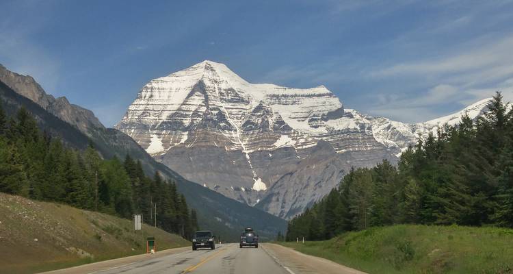 Le Mont-Robson aux pics enneigés domine une route flanquée d'une forêt de conifères dense.
