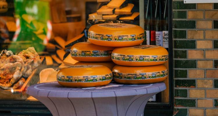 Stacks of round Gouda cheese wheels displayed outside a traditional Dutch shop window.