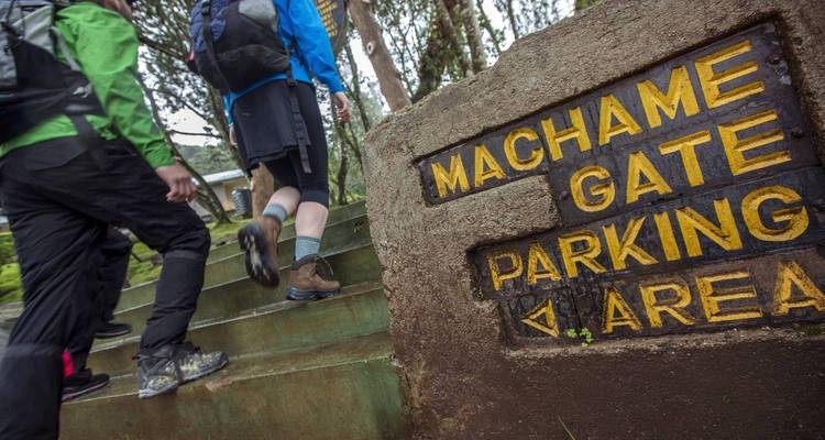 Menschen, die an einem Schild vorbeigehen, auf dem "Machame Gate Parking Area" steht.