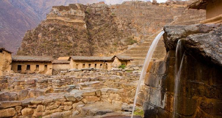 Alte Steinstrukturen mit fließendem Wasserelement, umgeben von Bergen.