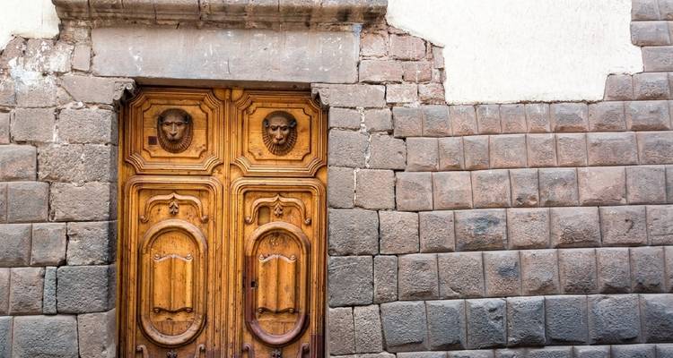 Verzierte Holztür in einer Steinmauer mit dekorativen Schnitzereien.