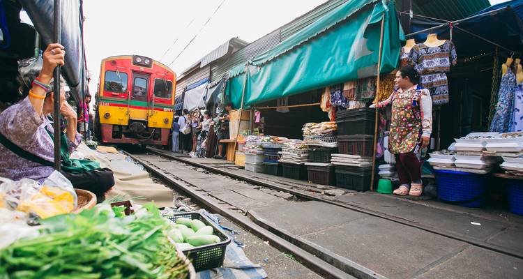 Le train jaune vif se faufile dans le marché ferroviaire de Maeklong tandis que les vendeurs se tiennent à côté de leurs étals.
