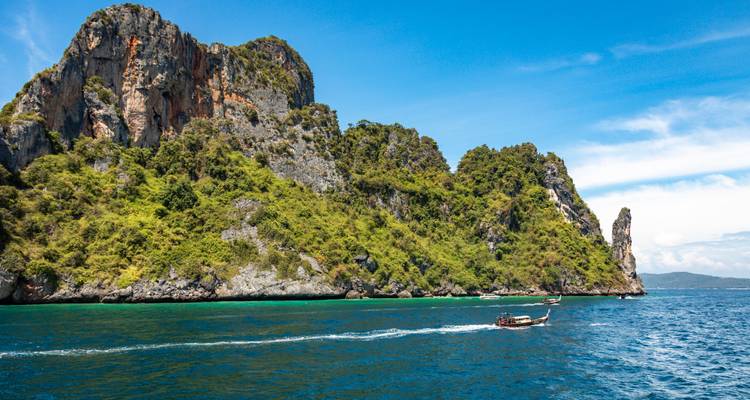 Le bateau à longue queue fonce sur les eaux bleu profond à côté de falaises imposantes couvertes de jungle.