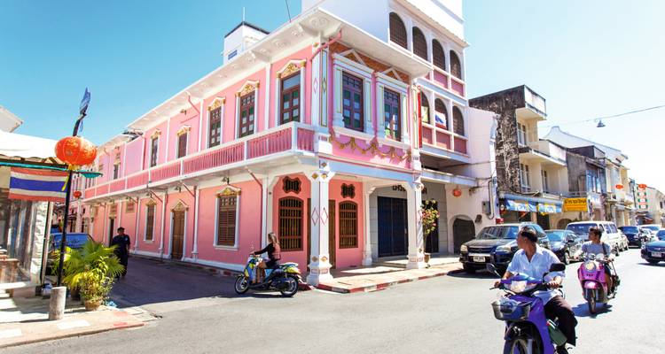 Bâtiment historique rose situé au coin d'une rue ensoleillée tandis que des habitants passent à motocyclette.