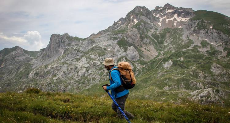 Randonneur traversant un terrain montagneux accidenté avec des plaques de neige.