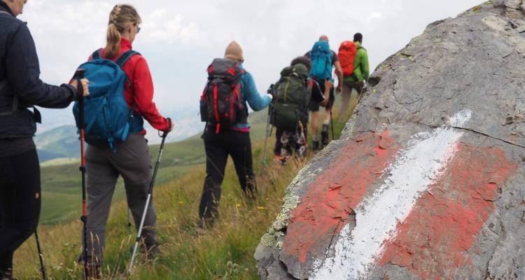 Groupe de randonneurs sur un sentier avec une borne en pierre peinte.