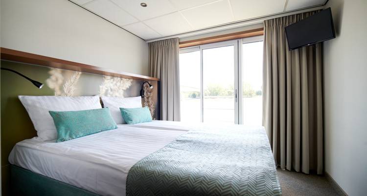 Vue intérieure d'une chambre d'hôtel moderne bien éclairée avec un lit et une grande fenêtre.