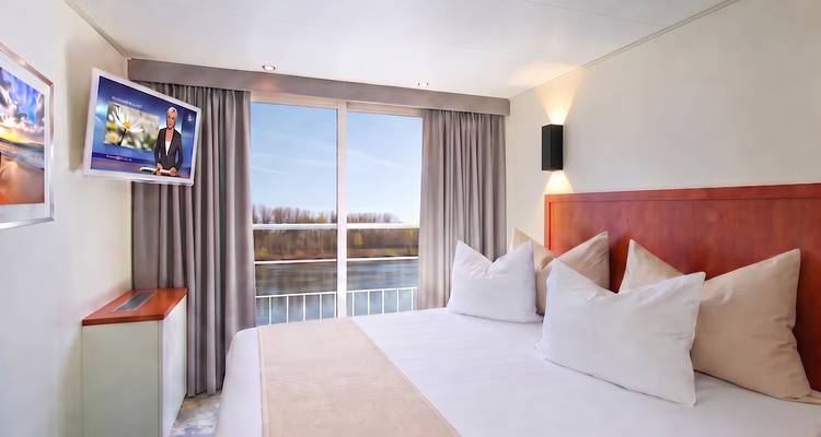 Bright river-view stateroom with balcony doors, flat-screen TV and plush bedding on a cruise ship.