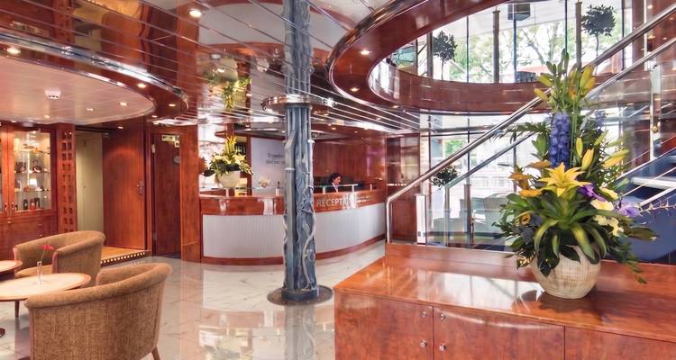 Glossy wood-paneled reception lobby of a river cruise ship with marble floors and flower arrangements.