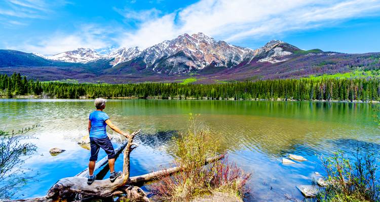 Person admiring a scenic mountain lake with snow-capped peaks.