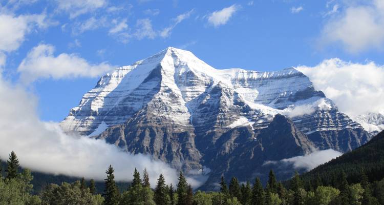 Snow-capped mountain landscape with clear blue skies and forests below.