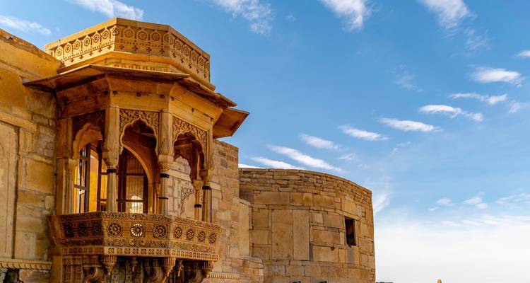 Sierlijk gebeeldhouwde balkon van een zandstenen gebouw onder een blauwe hemel.