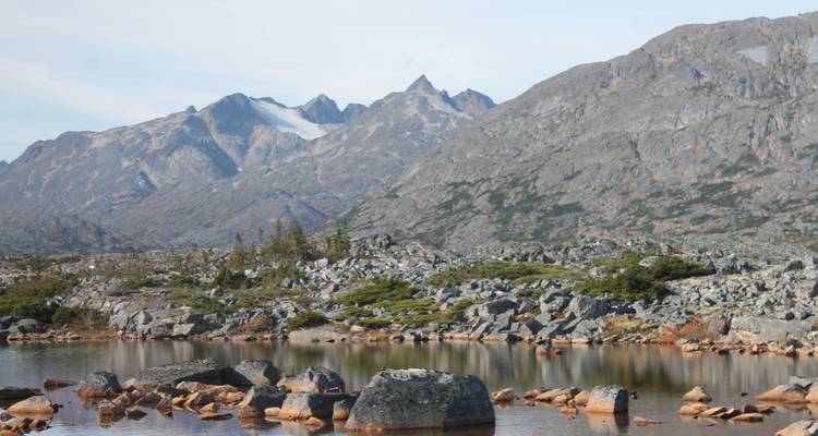 Rocky alpine landscape with jagged peaks and a small reflective tarn in the foreground.