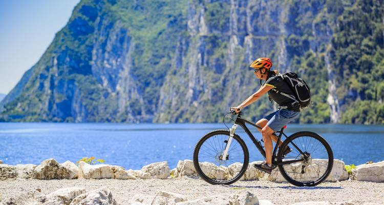Ein Radfahrer, der an einem See entlang fährt, mit Bergen im Hintergrund.