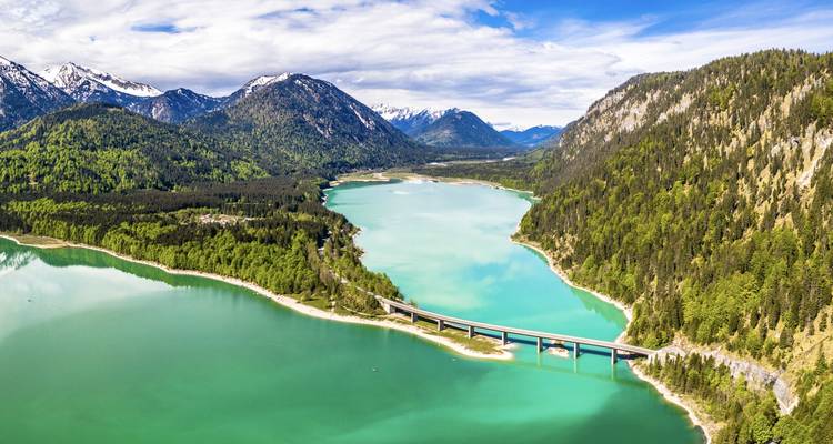 Vue aérienne d'une rivière avec un pont, entourée de montagnes.