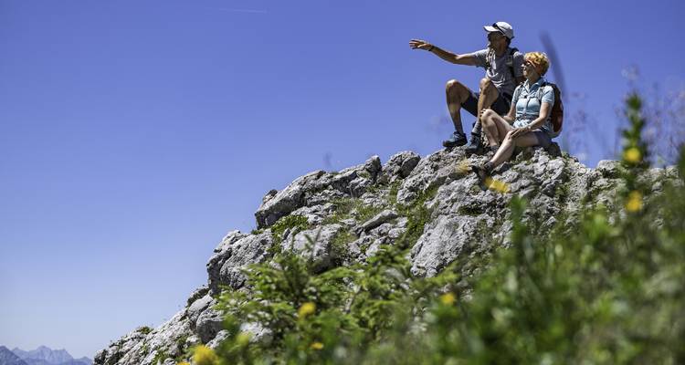 Two hikers sitting on a rock, admiring the view with blue sky.