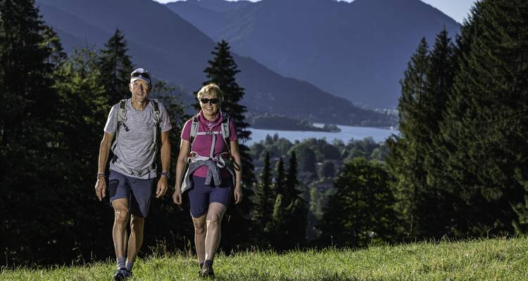Two hikers walking with a scenic mountain and lake view in the background.