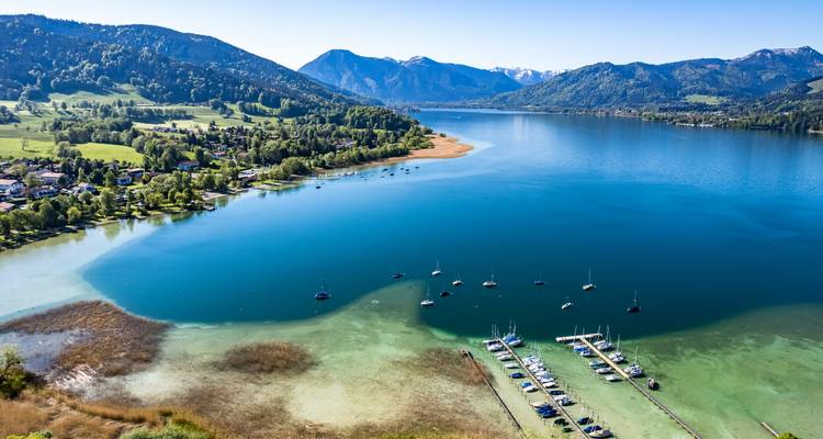 Aerial view of a lake with sailboats and mountains in the background.