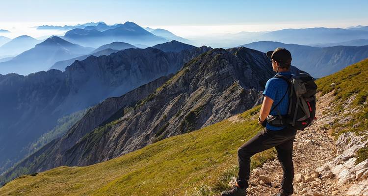 Wanderer, der eine dramatische Bergkette unter einem teilweise bewölkten Himmel überblickt.